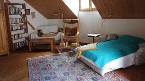 A cozy attic bedroom with a bed, a chair, a small table, a bookshelf, and a window.