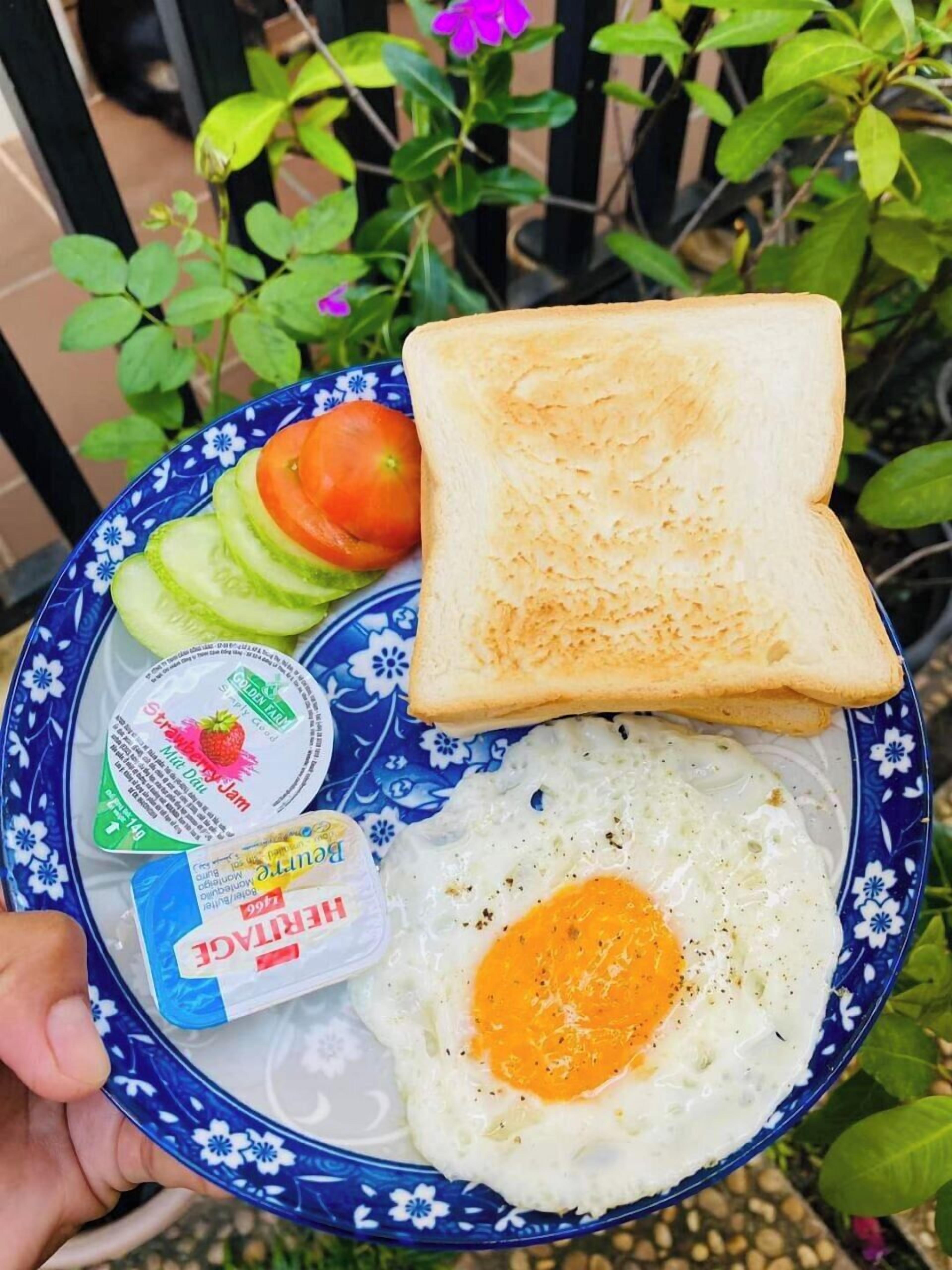Un plato con un huevo frito, rodajas de pepino, tomate y dos tostadas, sostenido por una mano.
