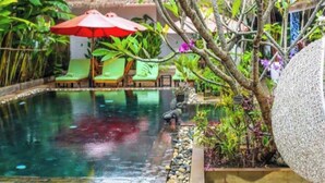 Un área de piscina interior tranquila con una estructura de piedra, sillones reclinables verdes y una sombrilla roja.