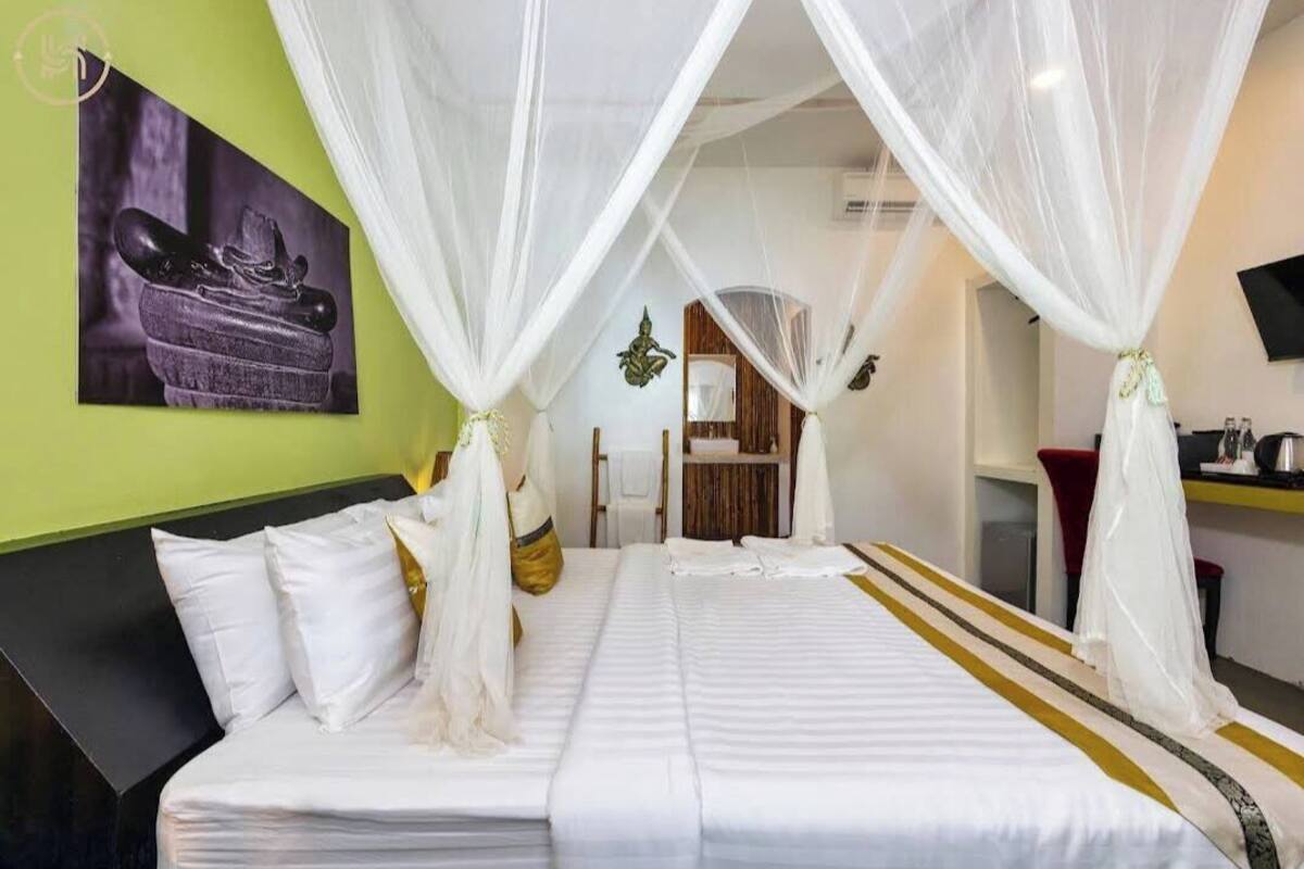 A hotel room with a bed, white curtains, a green wall, and a painting of shoes.