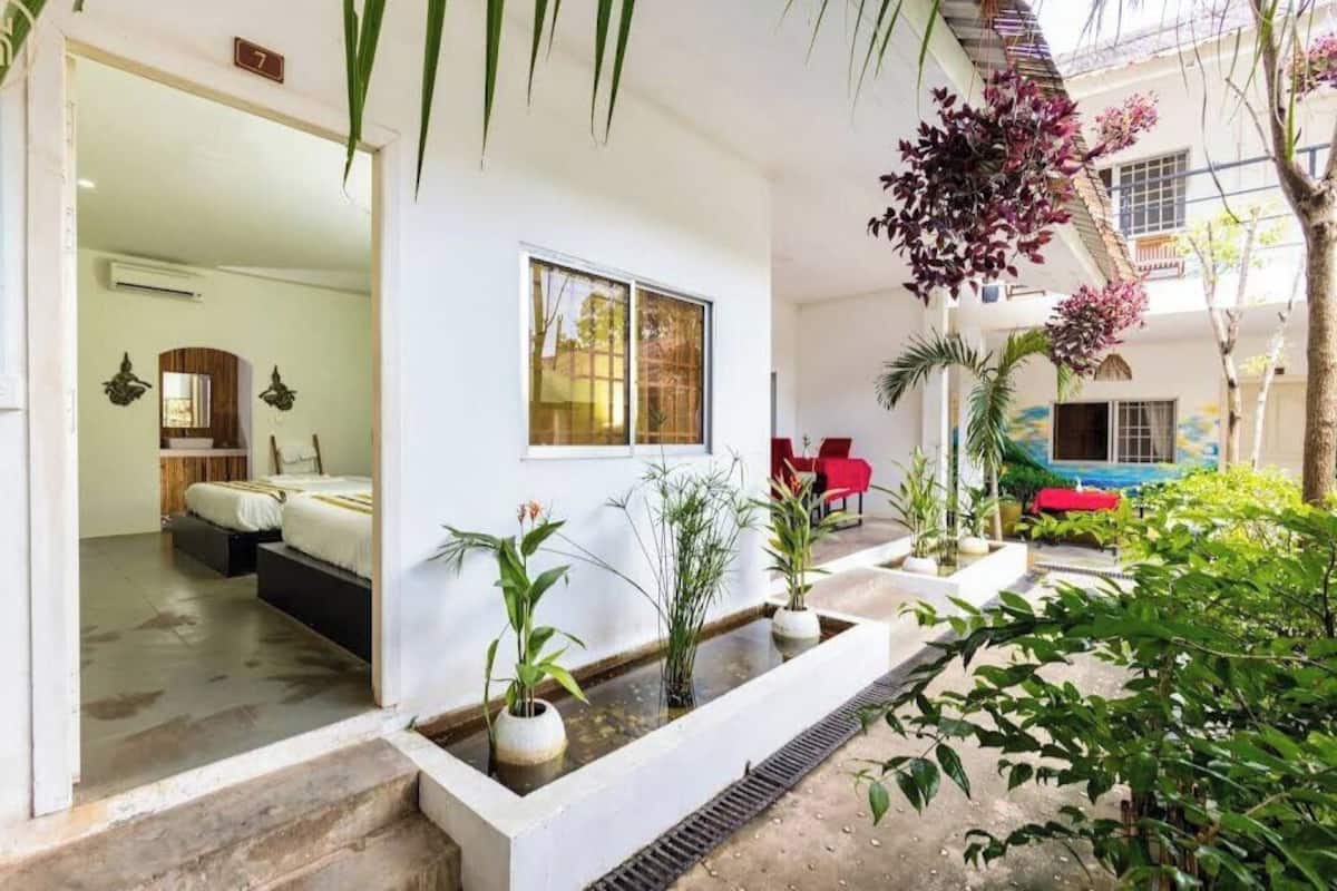 A modern hotel room with a large window, a bed, and a small balcony with potted plants.