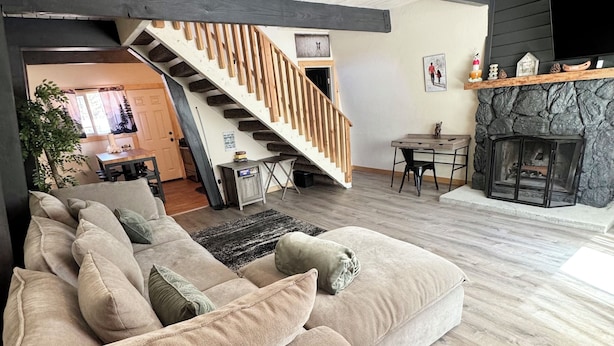 A spacious living area with a large beige sectional sofa, a wooden staircase, a stone fireplace, and a dining area with a table and chairs.