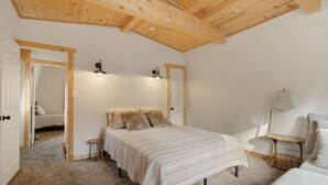 A bedroom with a wooden ceiling, a bed with a striped bedspread, two bedside lamps, and a small table with a lamp.