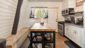A compact kitchen with a wooden table, black chairs, a stove, and a microwave.