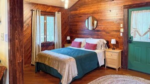 Un dormitorio de cabaña de madera con cama, mesitas de noche, un espejo y una puerta verde.
