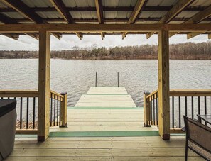 A wooden pier leading to a body of water with a covered seating area and a view of the shoreline.