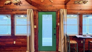 Una cabaña con paredes de madera, una puerta verde y ventanas con vistas a un cuerpo de agua.