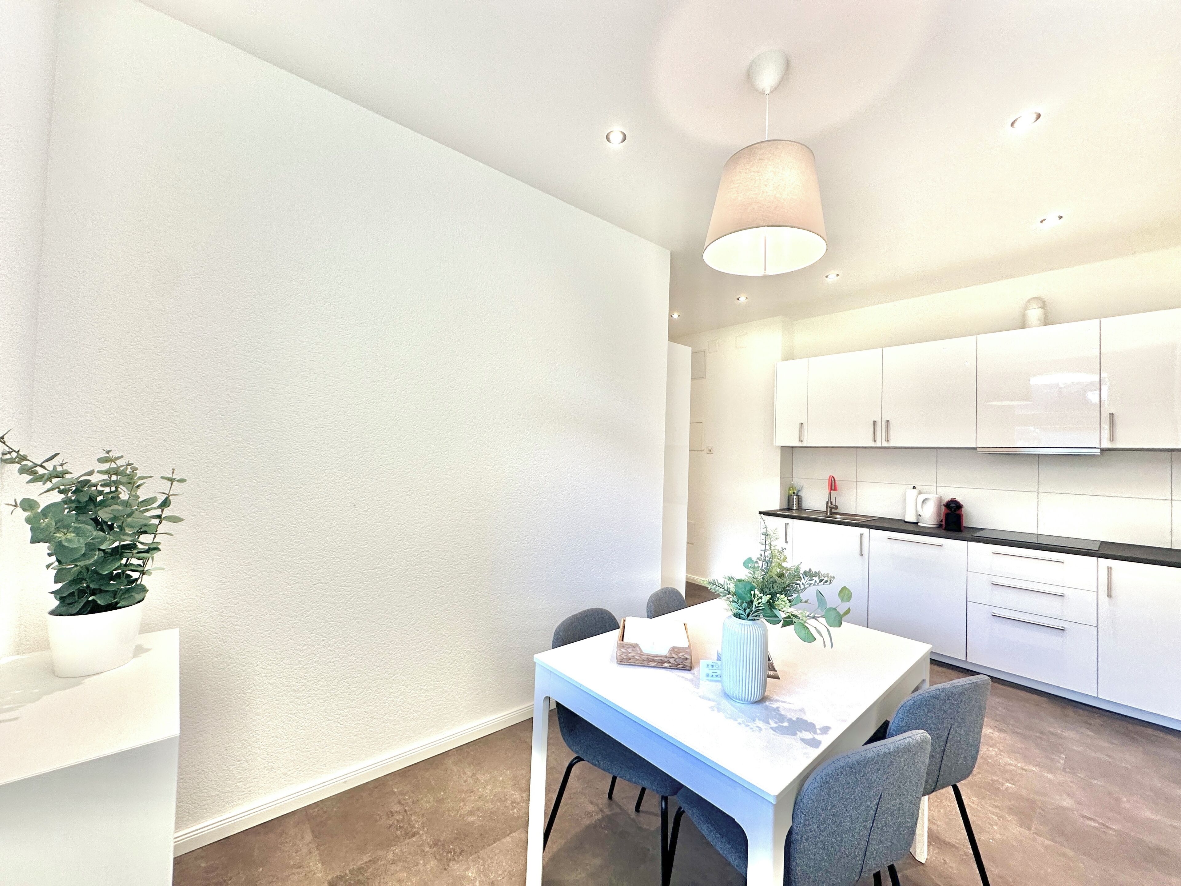 A modern kitchen with white cabinets, a white countertop, and a pendant light.