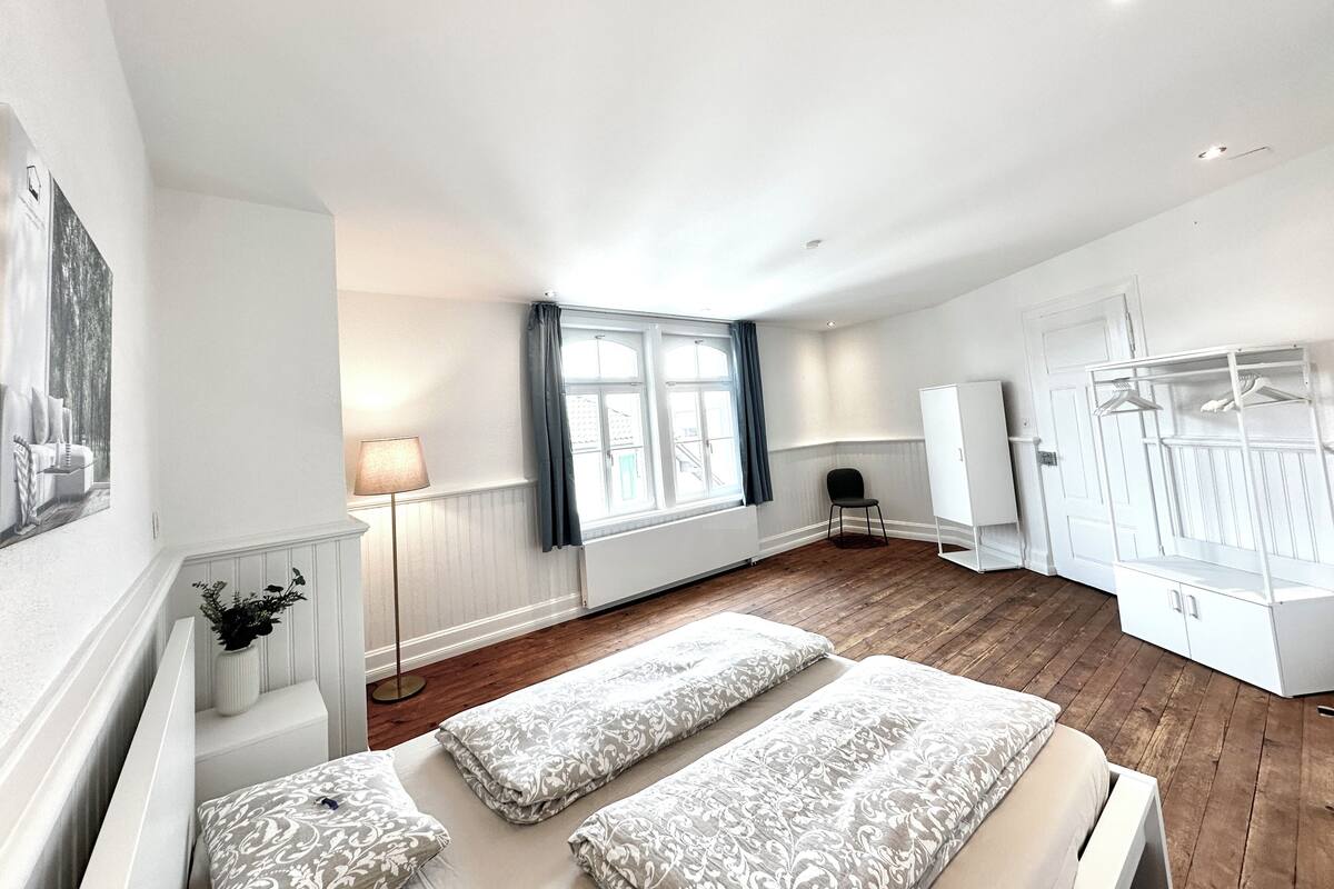 Una habitación amplia con un gran ventanal, una cama con ropa de cama estampada, una silla y un armario.