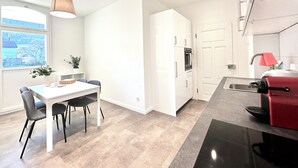 A modern kitchen with white cabinetry, a dining area with a table and chairs, and a red appliance on the counter. - Business Apartment Niederbipp (Niederbipp)