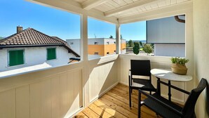 A balcony with a wooden floor, white walls, and a view of neighboring buildings. - Business Apartment Niederbipp (Niederbipp)