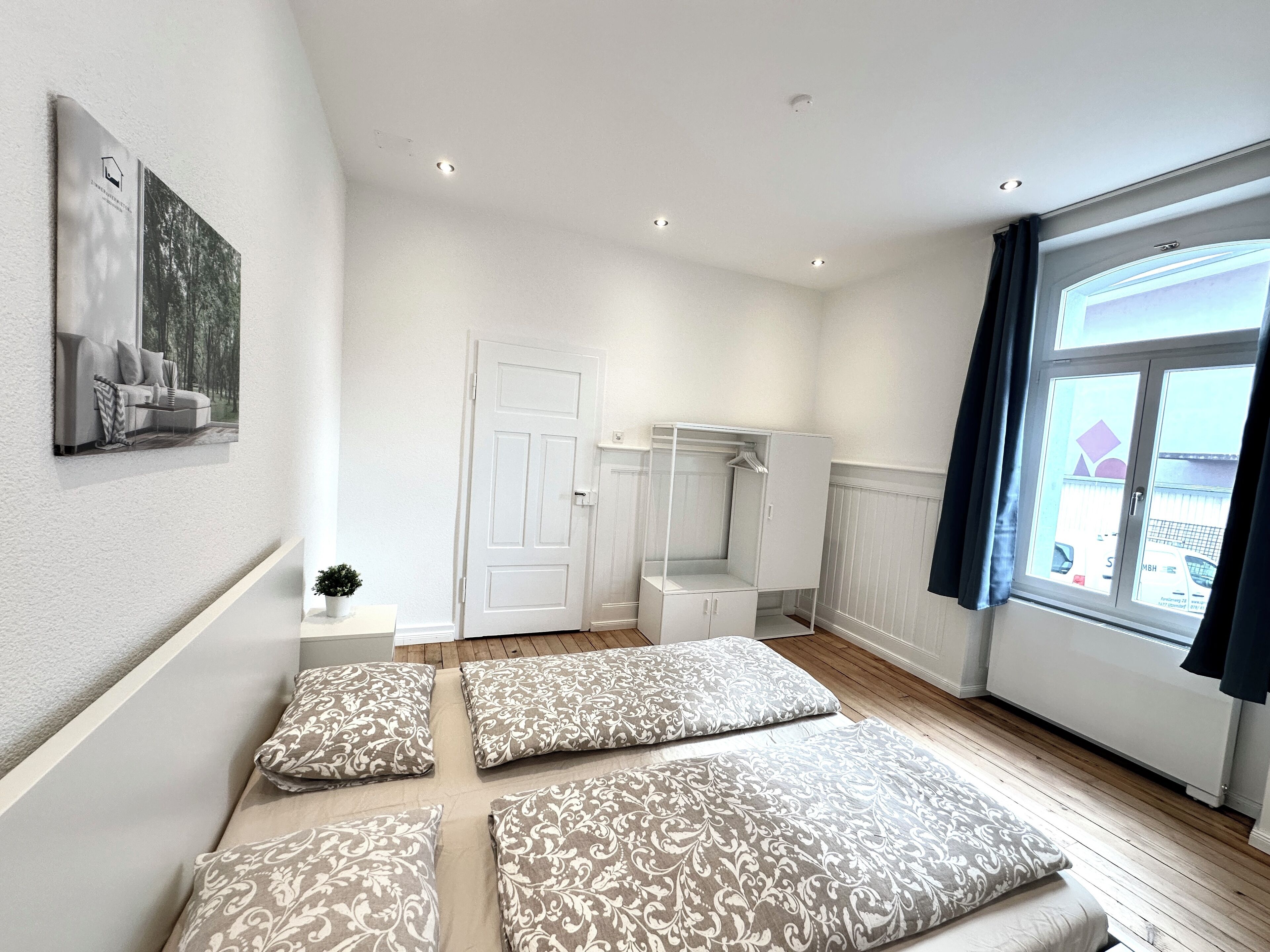 A modern bedroom with a large window, a wardrobe, and a bed with patterned pillows.