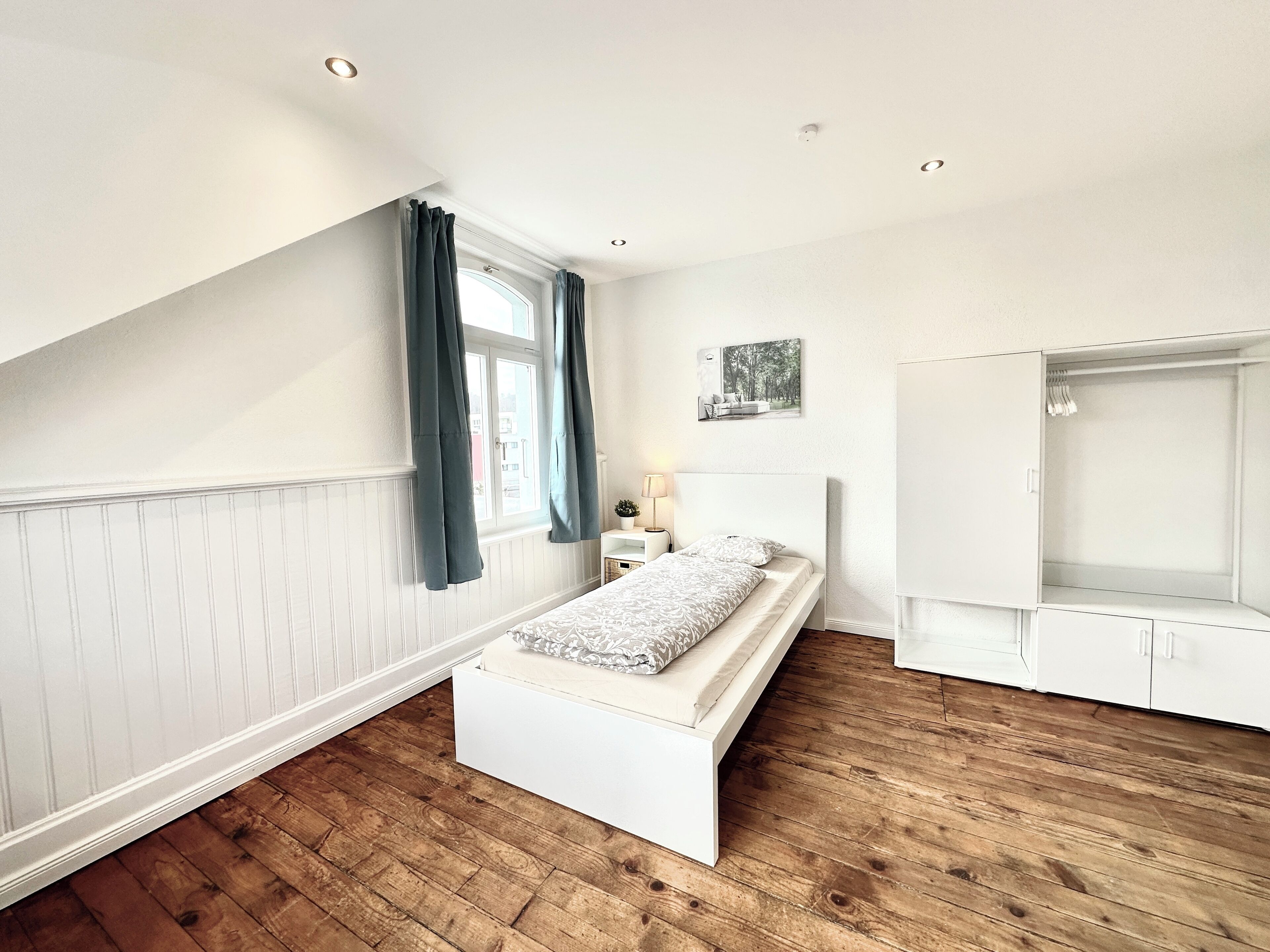 A bedroom with a bed, a nightstand, a dresser, a window with curtains, and a ceiling light.