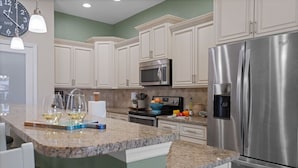 A kitchen with white cabinets, a stainless steel refrigerator, a microwave, and a granite countertop.