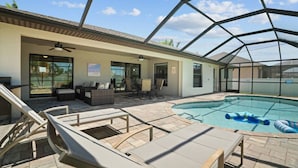 A covered outdoor swimming pool area with lounge chairs, a seating area, and a ceiling fan.