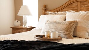 A neatly made bed with a black blanket, a tray with cups and a remote control, and a lamp on a bedside table.