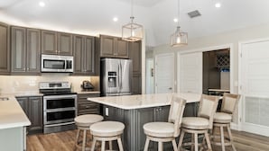 Una cocina moderna con electrodomésticos de acero inoxidable, una isla de mármol con taburetes altos y suelo de madera.