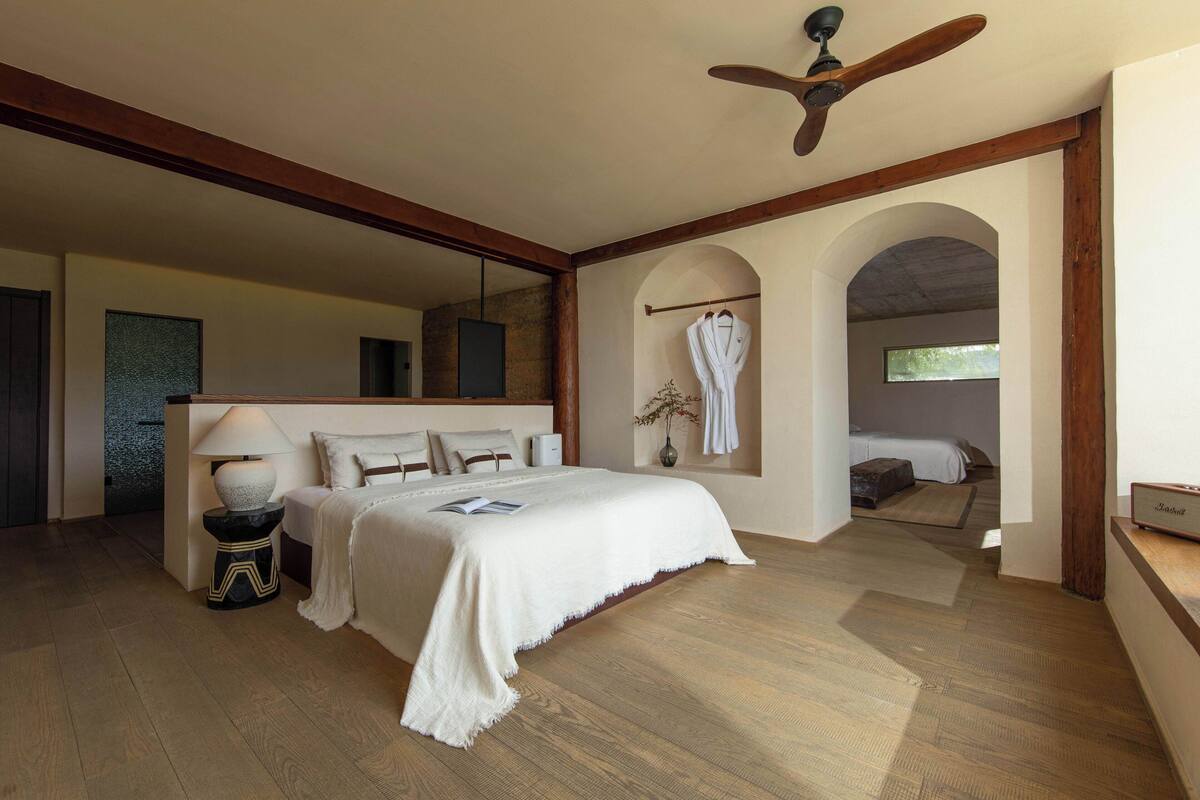A spacious bedroom with a large bed, a ceiling fan, and a view through an archway to another room.