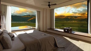A bedroom with a large bed, a ceiling fan, and a view of a mountainous landscape through large windows. - Liz's heart is in the sky (Deqin)