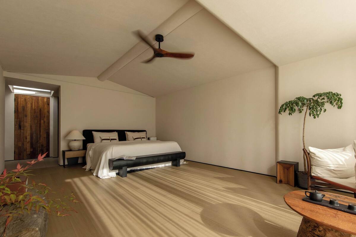 A modern bedroom with a bed, bedside table, lamp, and a ceiling fan.