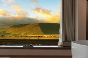 A room with a large window offering a view of a mountain and a field. - Liz's heart is in the sky (Deqin)