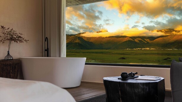 A modern hotel room with a large window offering a view of a mountainous landscape. - Liz's heart is in the sky (Deqin)