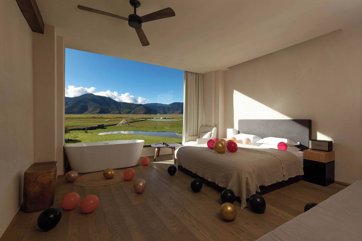 A bedroom with a large window, a bathtub, and balloons on the floor.