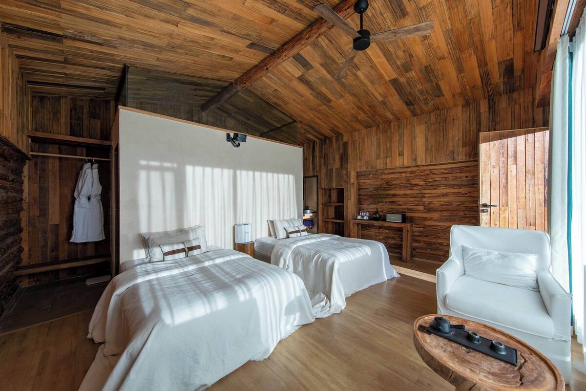 A wooden cabin-style room with two beds, a white sofa, and a wooden coffee table.