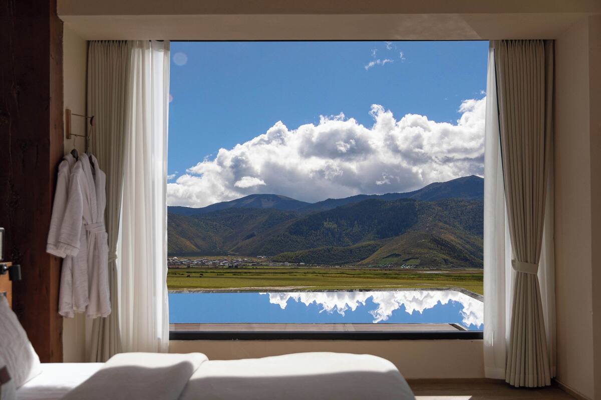 A room with a large window offering a view of mountains and a lake.
