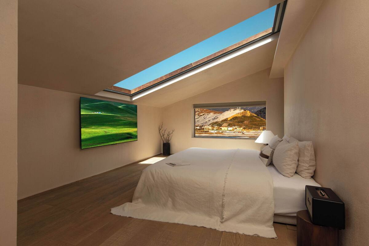 A bedroom with a skylight, a bed, a nightstand, and two paintings.