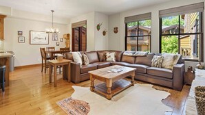 A spacious living room with a brown leather sofa, wooden coffee table, and a dining area with a wooden table and chairs. - SkiView Luxury Townhome - Steps to Ketchum + Skiing, Dog-Friendly! (Ketchum)