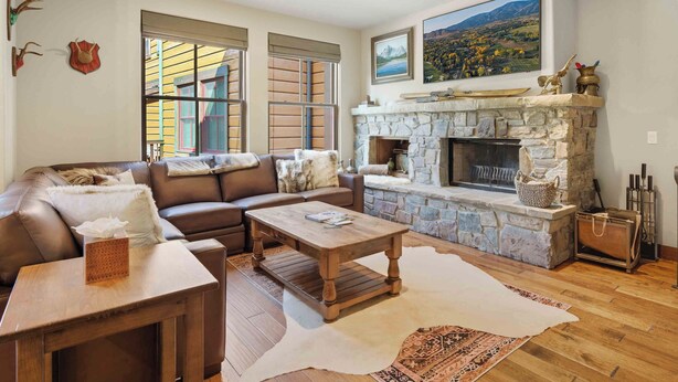 A cozy living room with a stone fireplace, leather sofa, and a large window with shutters. - SkiView Luxury Townhome - Steps to Ketchum + Skiing, Dog-Friendly! (Ketchum)