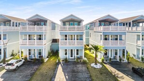 A beachfront multi-story building with balconies, a paved driveway, and a small lawn area.