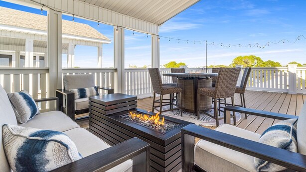 A covered outdoor patio with a fire feature, seating, and string lights.