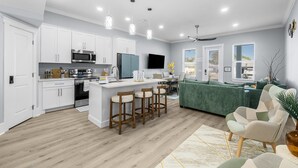 A modern kitchen with white cabinets, a central island with bar stools, a built-in oven, and a microwave.