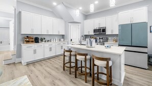 A modern kitchen with white cabinets, a central island with stools, a large refrigerator, and a microwave.