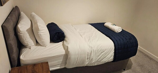 A single bed with a grey headboard, white bedding, and a dark blue blanket.