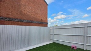 A fenced backyard with artificial grass, a brick wall, and a white fence. - House - Sleeps 8 - Parking - Station Close (Wolverhampton)