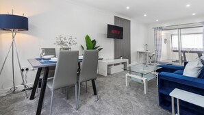 Una sala de estar moderna con comedor, televisor montado en la pared y un sofá azul.