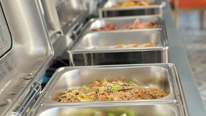 Una barra de buffet con diversas opciones de comida, incluyendo una sección con verduras y fideos.