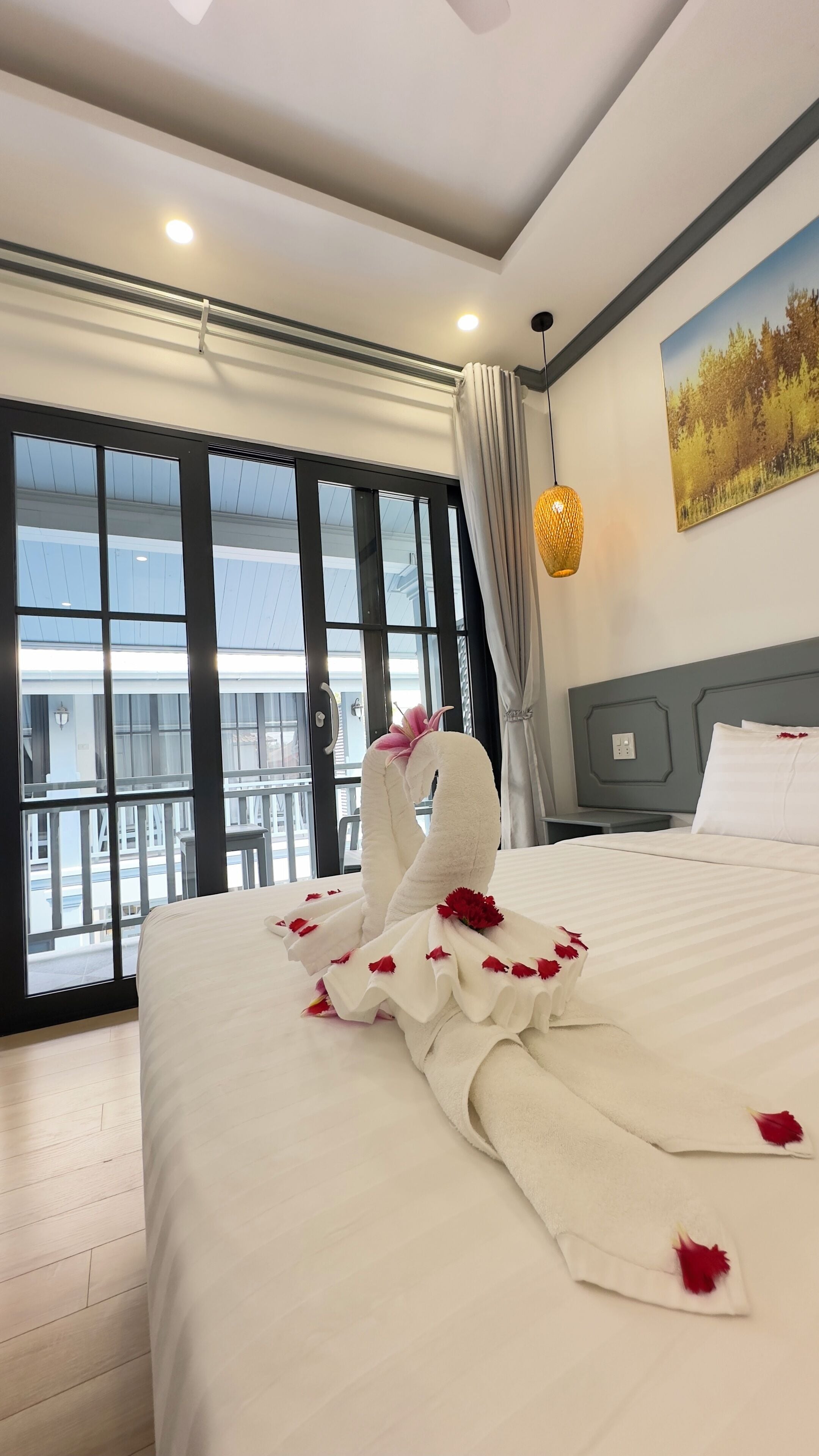 A hotel room with a large bed, a view of a balcony, and a painting on the wall.
