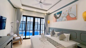 Habitación de hotel con cama, escritorio, silla, televisión, ventilador de techo y ventana grande con vistas a una piscina y zona de estar al aire libre.