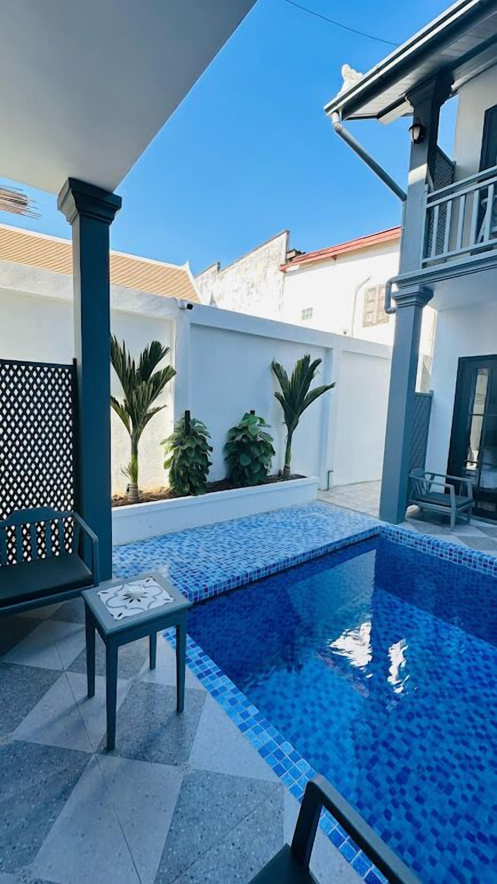 Una piscina con borde de azulejos, una banca y plantas en macetas.