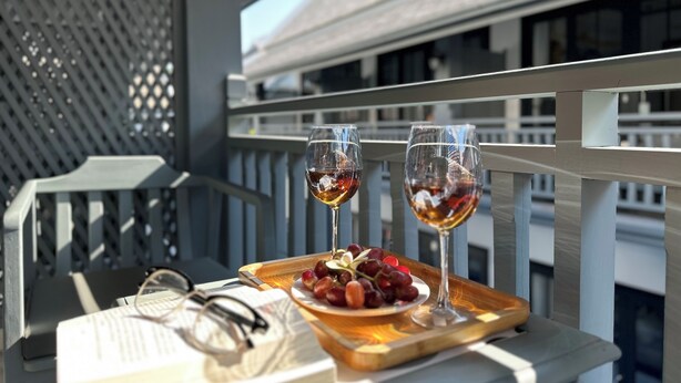 Un balcón con dos copas de vino, un plato de uvas y un par de gafas sobre una bandeja.