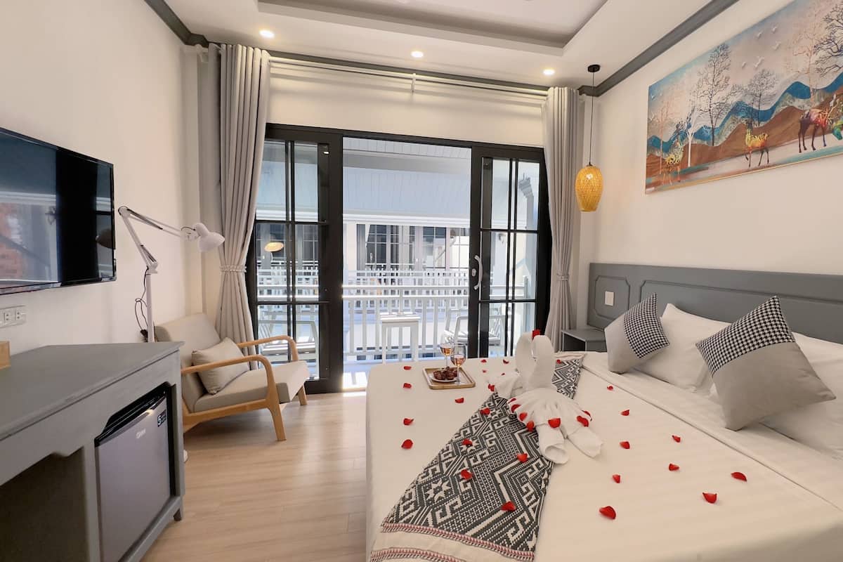 A hotel room with a bed, a desk, a chair, a TV, and a balcony view.
