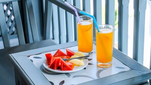 Una mesa con dos vasos de jugo de naranja y un plato de rebanadas de sandía y piña en un balcón.