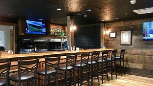 A bar area with a long counter, multiple stools, and a television mounted on the wall. - Treetop Retreat in Connestee Falls (Brevard)