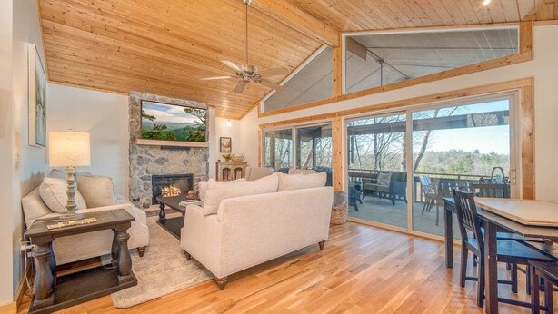 A spacious living room with a fireplace, wooden ceiling, and large sliding glass doors leading to an outdoor area. - Treetop Retreat in Connestee Falls (Brevard)