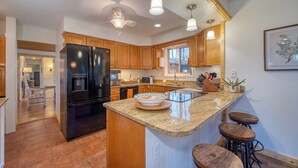 A modern kitchen with a large island, wooden cabinets, and a black refrigerator. - Treetop Retreat in Connestee Falls (Brevard)