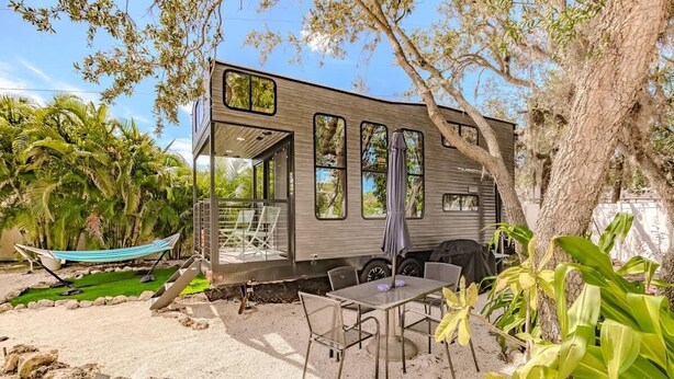 A modern RV with a covered patio area, outdoor seating, and a hammock.